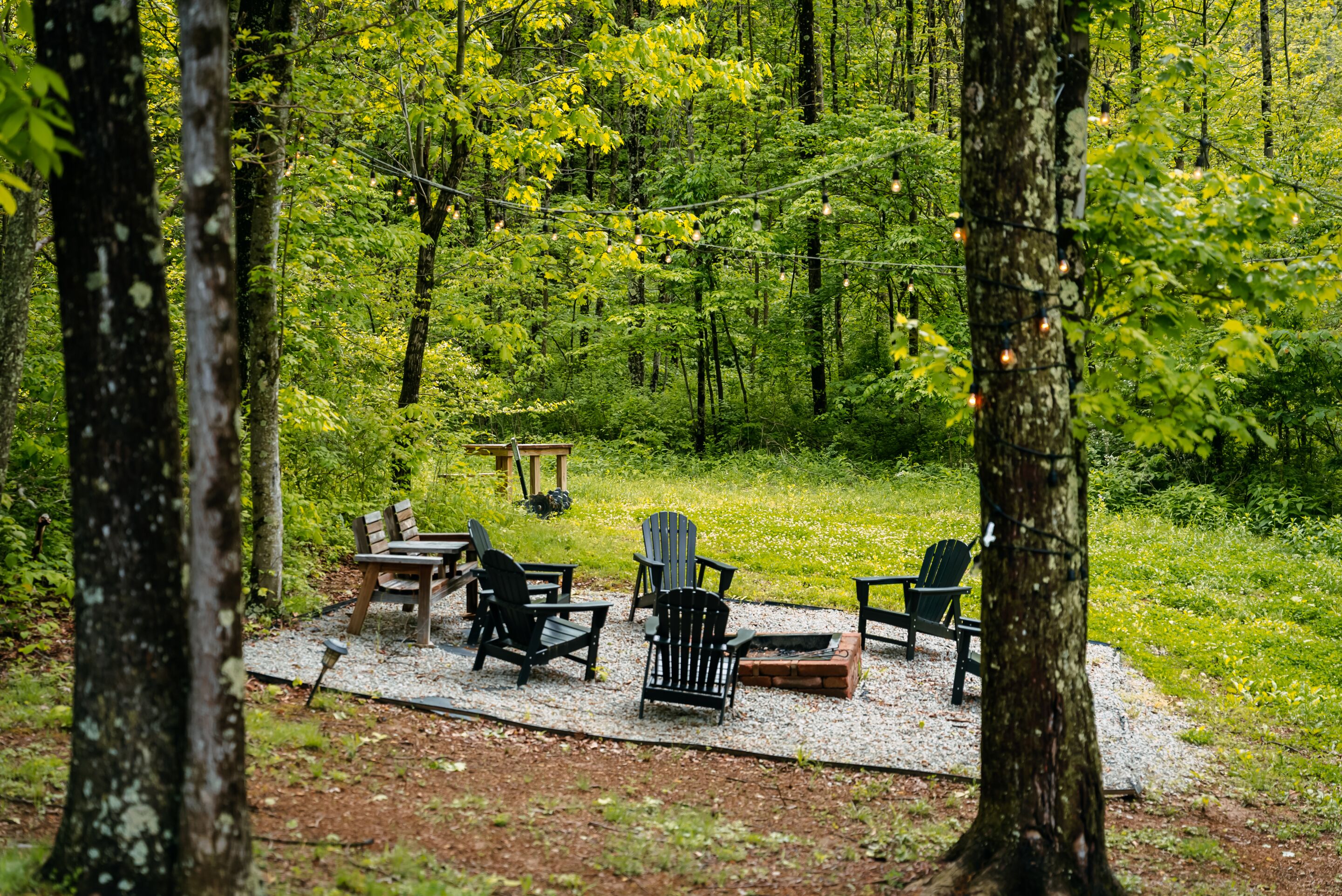 A forested area with outdoor seating including chairs and a table, surrounded by trees.