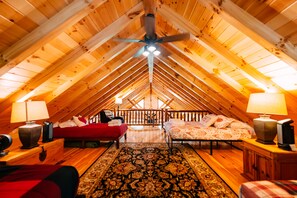 Ein Schlafzimmer im Dachgeschoss mit geneigter Decke, zwei Betten, einem Deckenventilator und einem gemusterten Teppich.