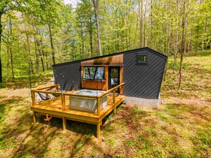 Une cabane dotée d’une terrasse en bois, d’un jacuzzi et d’un petit bâtiment attenant.
