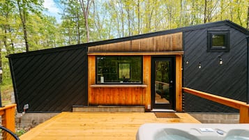 Uma cabana moderna com deck de madeira, hidromassagem e uma grande janela.