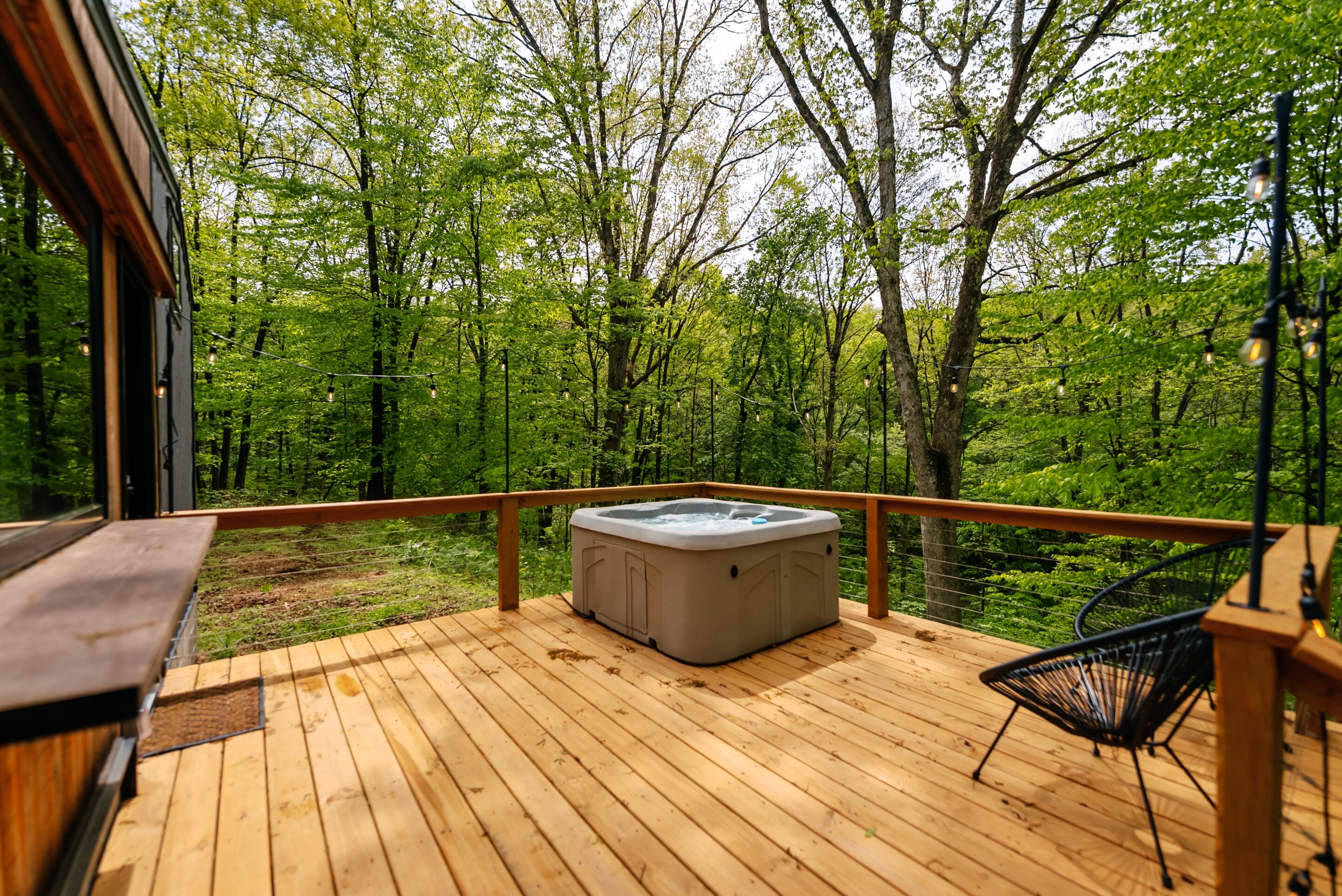 Terraza de madera con jacuzzi, una silla y vista a un bosque.