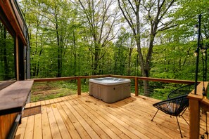 Une terrasse en bois avec un jacuzzi, une chaise et une vue sur une forêt.