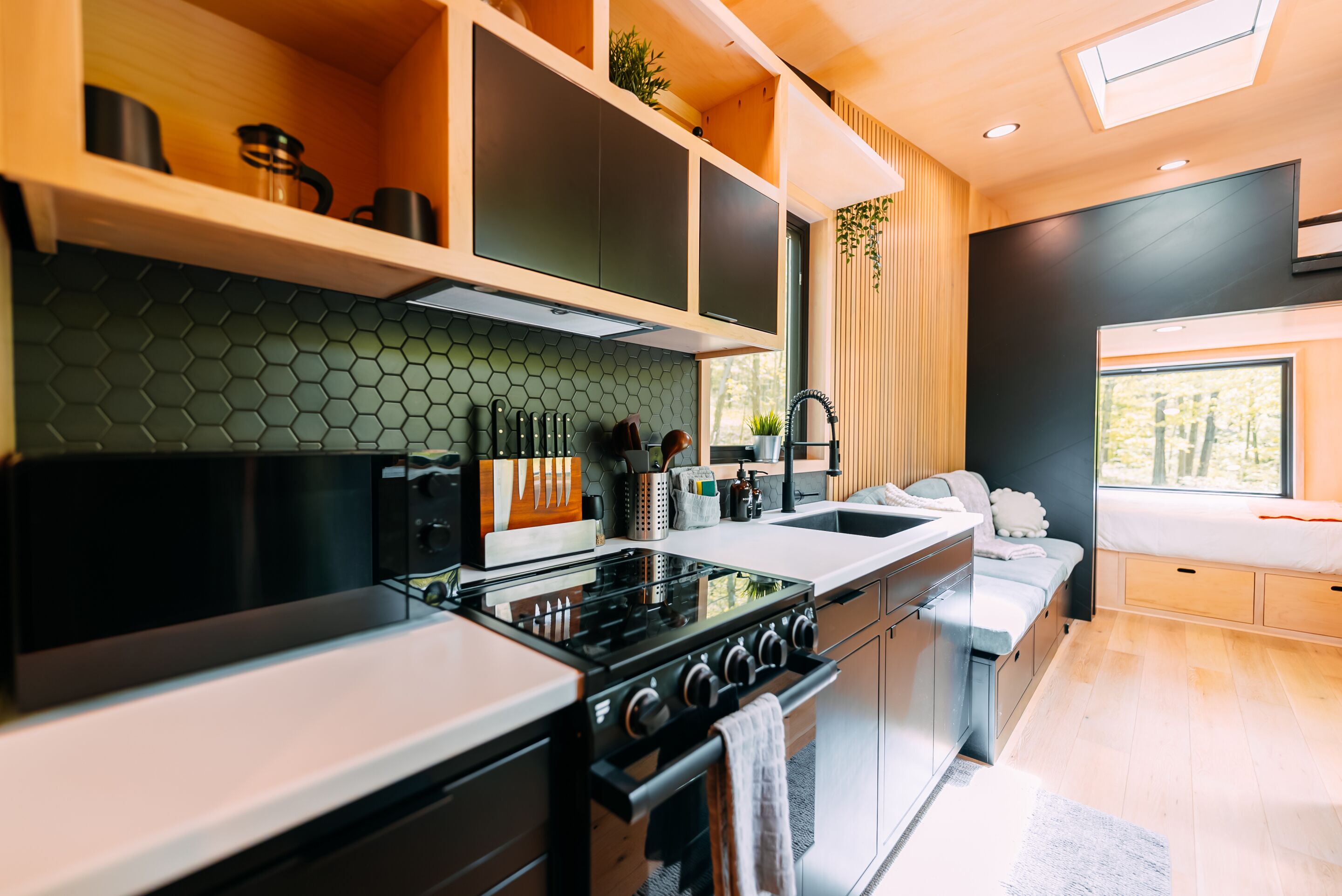 Une cuisine moderne équipée d’une cuisinière, d’un four et d’un plan de travail. Une fenêtre offre une vue sur les arbres.