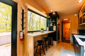 A modern kitchen with wooden cabinetry, a large window, and a bar area with stools. - Sangja | Hocking Hills, 60 Acres, Modern, Hot Tub (Logan)