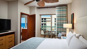 Ett hotellrum med en säng, en tv, ett skrivbord och utsikt över havet från balkongen.
