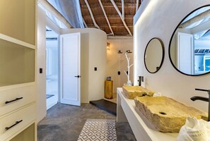 Une salle de bain moderne avec un grand miroir, deux lavabos et un tabouret en bois.