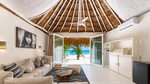 A beachside room with a thatched roof, a sofa, a coffee table, and a view of the beach. - Hotel Qamar Lux (Tulum)