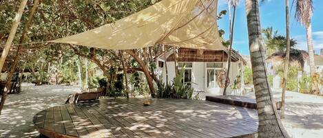 A wooden deck with a canopy, surrounded by palm trees and tropical vegetation.