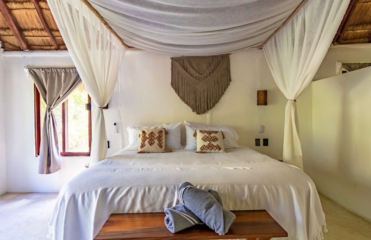 A bedroom with a bed, curtains, a wall hanging, and a bench.