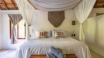 A bedroom with a bed, curtains, a wall hanging, and a bench.