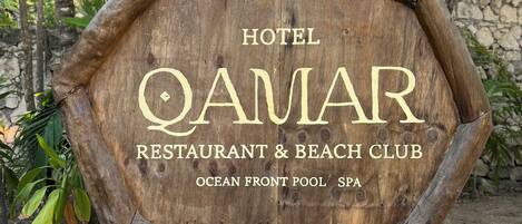 A wooden sign for Hotel Qamar, Restaurant & Beach Club, Ocean Front Pool SPA.