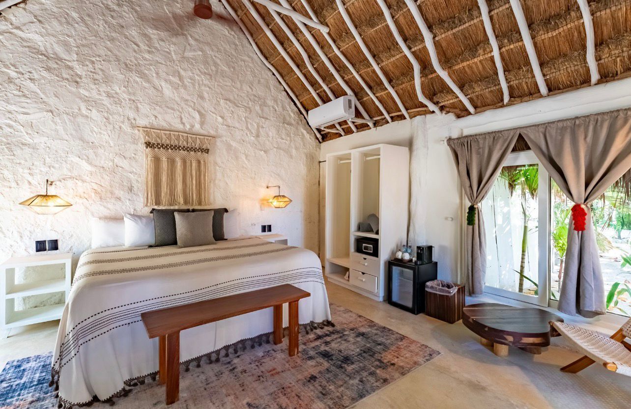 A bedroom with a bed, bedside tables, a bench, a TV, and a window with curtains.