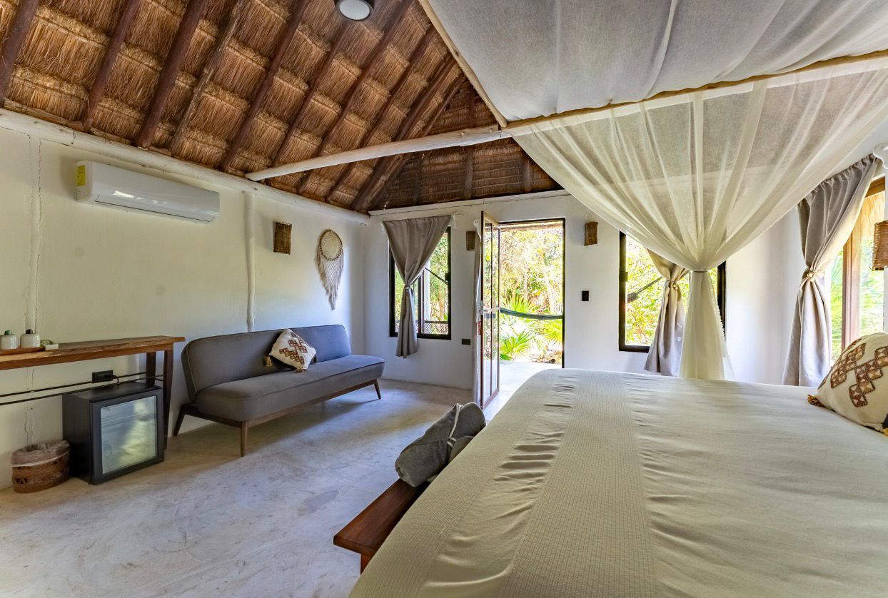 A bedroom with a bed, a sofa, a small table, a TV, and a balcony with curtains.