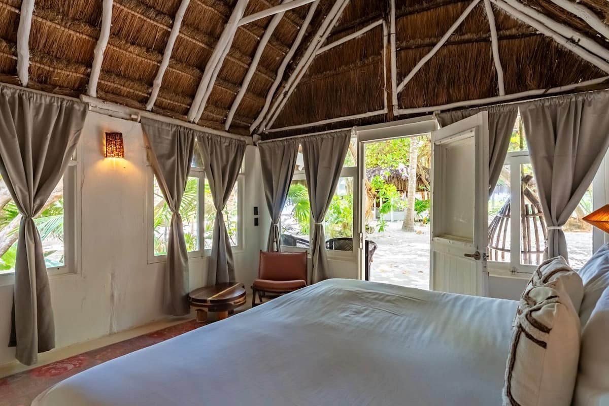 Une chambre avec un lit, des rideaux, une chaise et une vue sur la verdure.