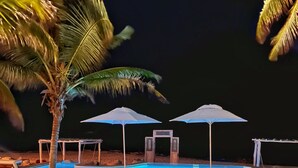 A nighttime poolside area with lounge chairs and umbrellas, a palm tree, and a clear pool. - Hotel Qamar Lux (Tulum)
