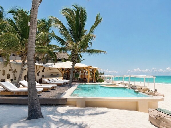Zona junto a la piscina con sillones de descanso, piscina y vista a la playa.