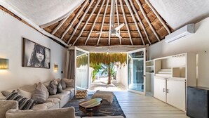 A spacious living area with a thatched ceiling, a sofa set, a coffee table, and a view of the outdoors. - Hotel Qamar Lux (Tulum)