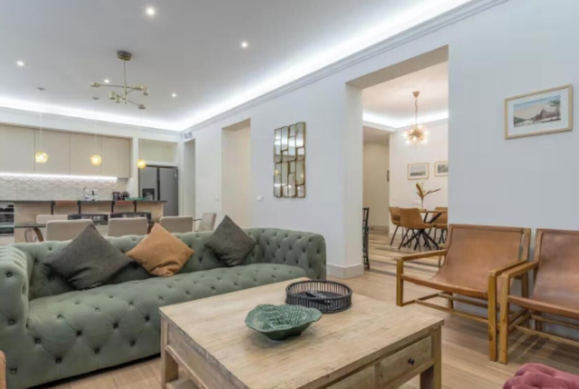 A modern living room with a green sofa, wooden coffee table, and a dining area with a wooden table and chairs.