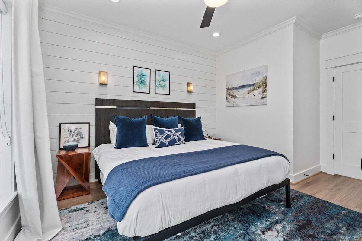 A bedroom with a bed, a nightstand, a wall-mounted light, and a painting.