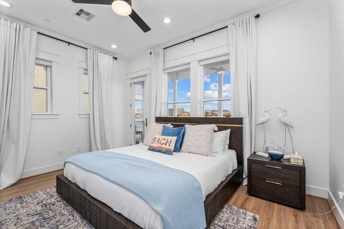 A bedroom with a bed, a nightstand, a ceiling fan, and a window with curtains.