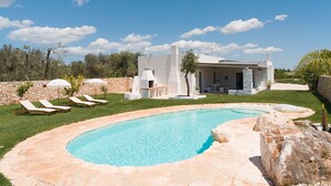 Une piscine avec des chaises longues, un mur en pierre et un bâtiment doté d’une terrasse.