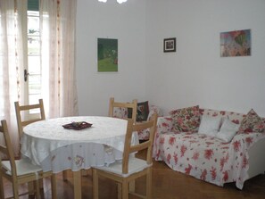 Uma sala de jantar com uma mesa redonda e cadeiras, um sofá com estofamento floral e duas obras de arte emolduradas na parede.