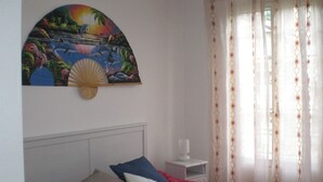 A bedroom with a red bedspread, a white headboard, and a painting of a tropical scene above the bed. - Charming marine living room accommodation in San Remo (Sanremo)