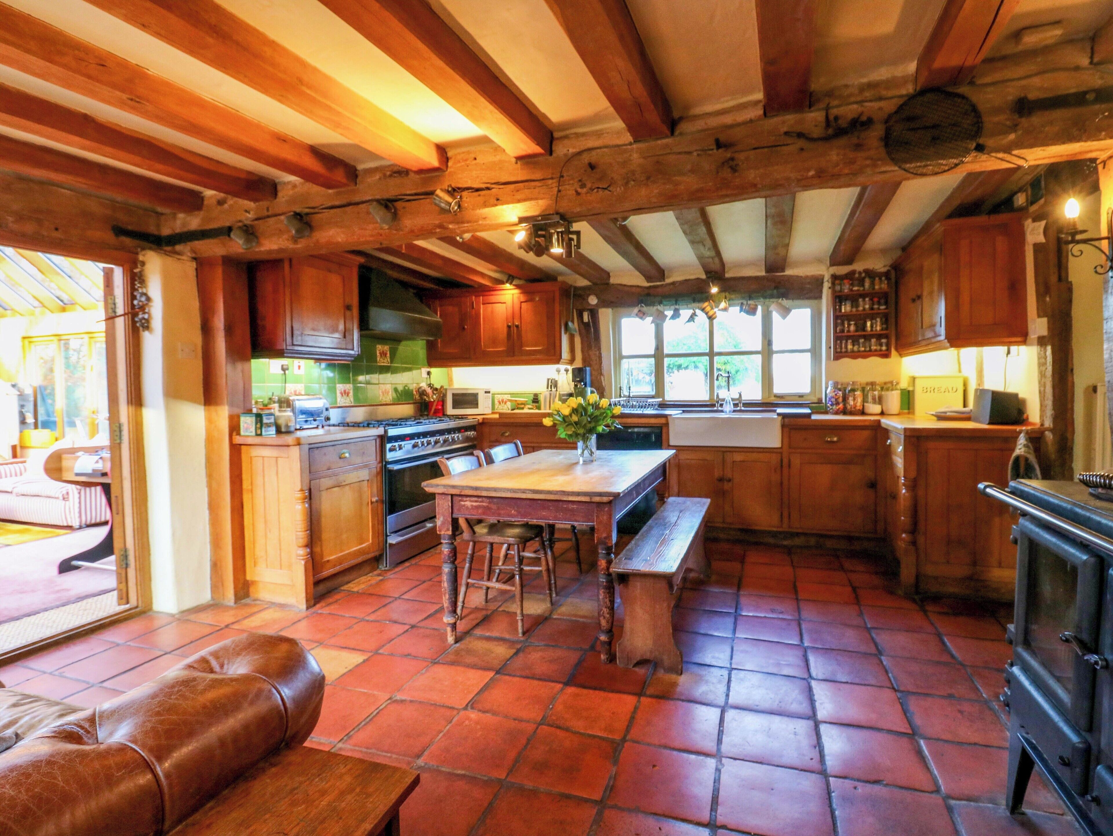 A rustic kitchen with wooden beams, a large stove, and a dining area with a bench and stools.