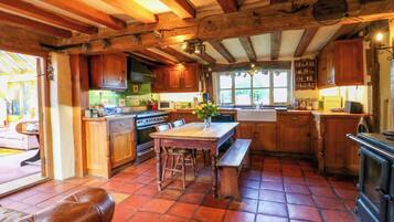 A rustic kitchen with wooden beams, a large stove, and a dining area with a bench and stools.