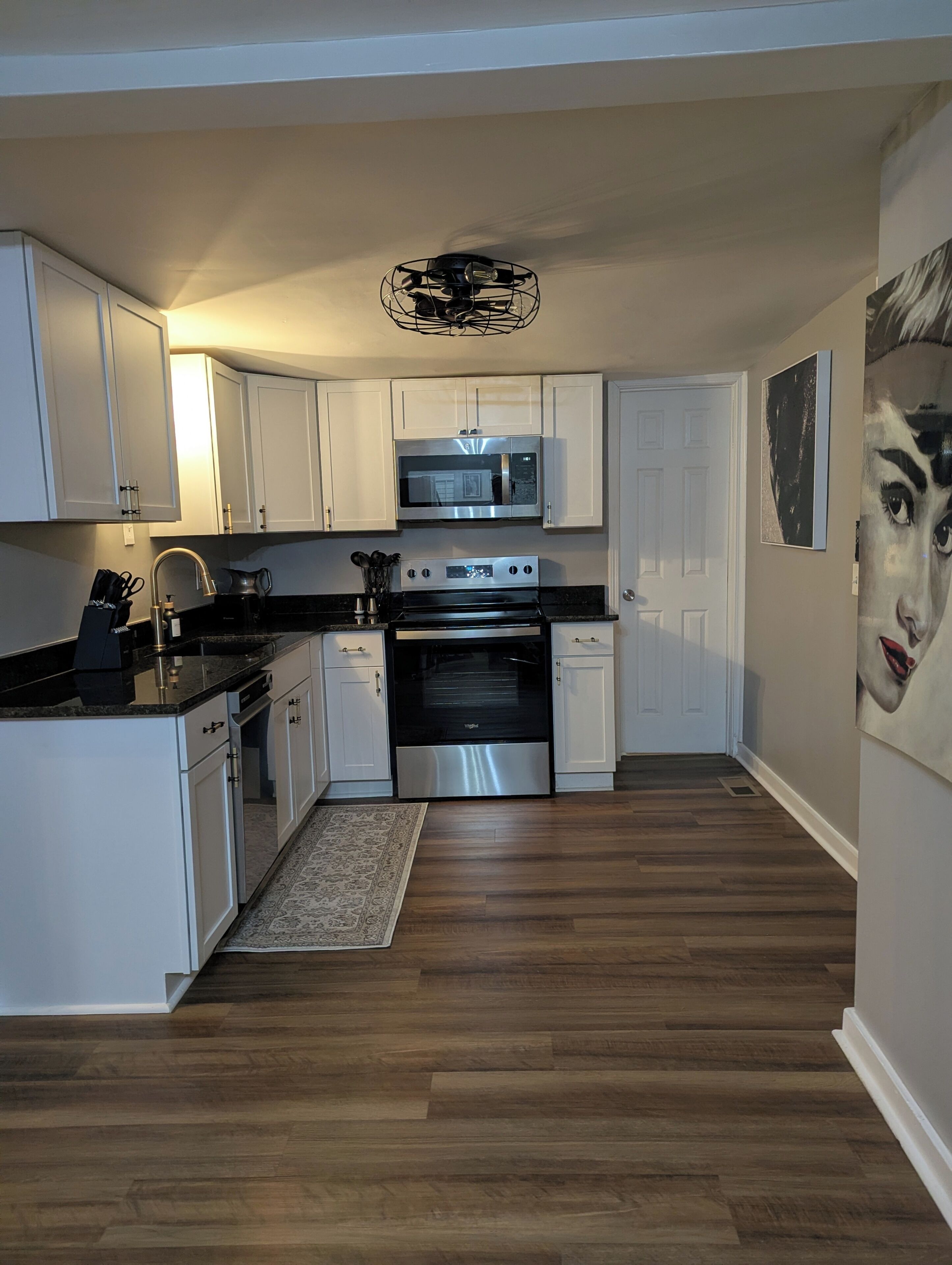 A modern kitchen with white cabinetry, stainless steel appliances, and a wooden floor.