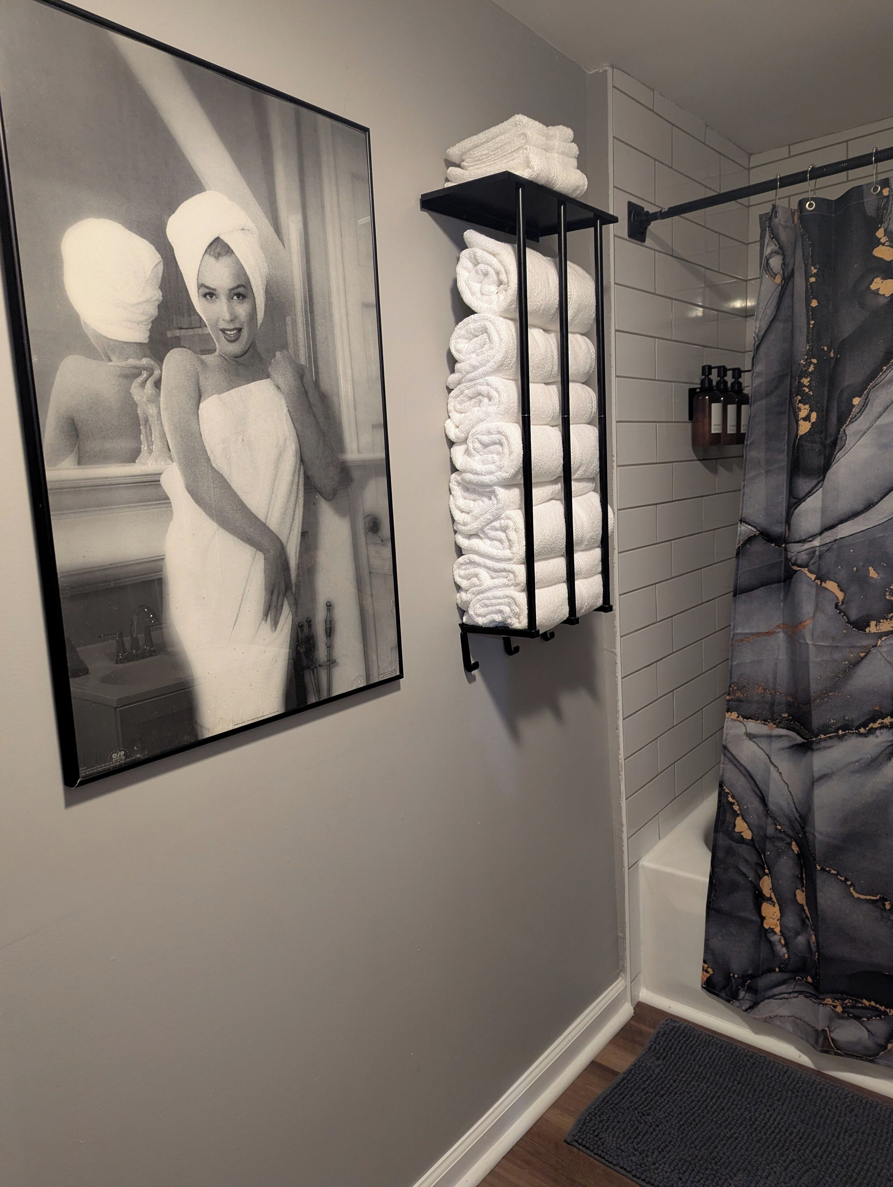 Une salle de bain avec une photographie en noir et blanc encadrée, un porte-serviettes avec des serviettes soigneusement pliées et un rideau de douche à motifs floraux.