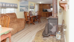 Een woonkamer met een bank, eettafel, stoelen, een open haard en een keuken op de achtergrond.