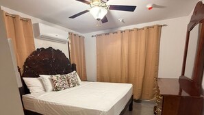 Een slaapkamer met een bed, een plafondventilator, gordijnen, een dressoir en een spiegel.