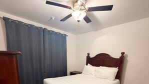 Een slaapkamer met een bed, houten hoofdbord, plafondventilator, nachtkastje en een kledingkast.