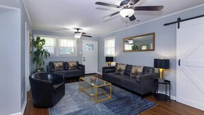 A living room with a sofa set, a coffee table, a floor lamp, a ceiling fan, and a large mirror. - Comfortable 2BR for Longer Stays in The Plaza / Noda Area (Charlotte)
