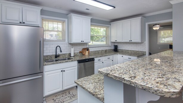 A modern kitchen with white cabinets, stainless steel appliances, granite countertops, and a large island. - Comfortable 2BR for Longer Stays in The Plaza / Noda Area (Charlotte)