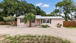 A single-story house with a metal roof, a small porch, and a gravel driveway. - pet friendly mid-century cottage near beaches (Fort Walton Beach)