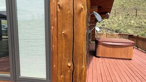 A wooden cabin with a large window, a deck, and a hot tub. - Beautiful 2-bedroom cabin with AC in cozy Cotopaxi with amazing views! (Cotopaxi)