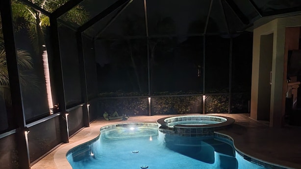 A swimming pool with a curved design, surrounded by a covered area with glass walls. - Charming 3-bedroom pool house in Sarasota, 5-minutes from Siesta Key beach (Sarasota)