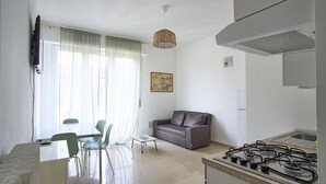 Een moderne keuken met een gasfornuis, een eethoek met een tafel en stoelen, een bank en een groot raam met gordijnen.