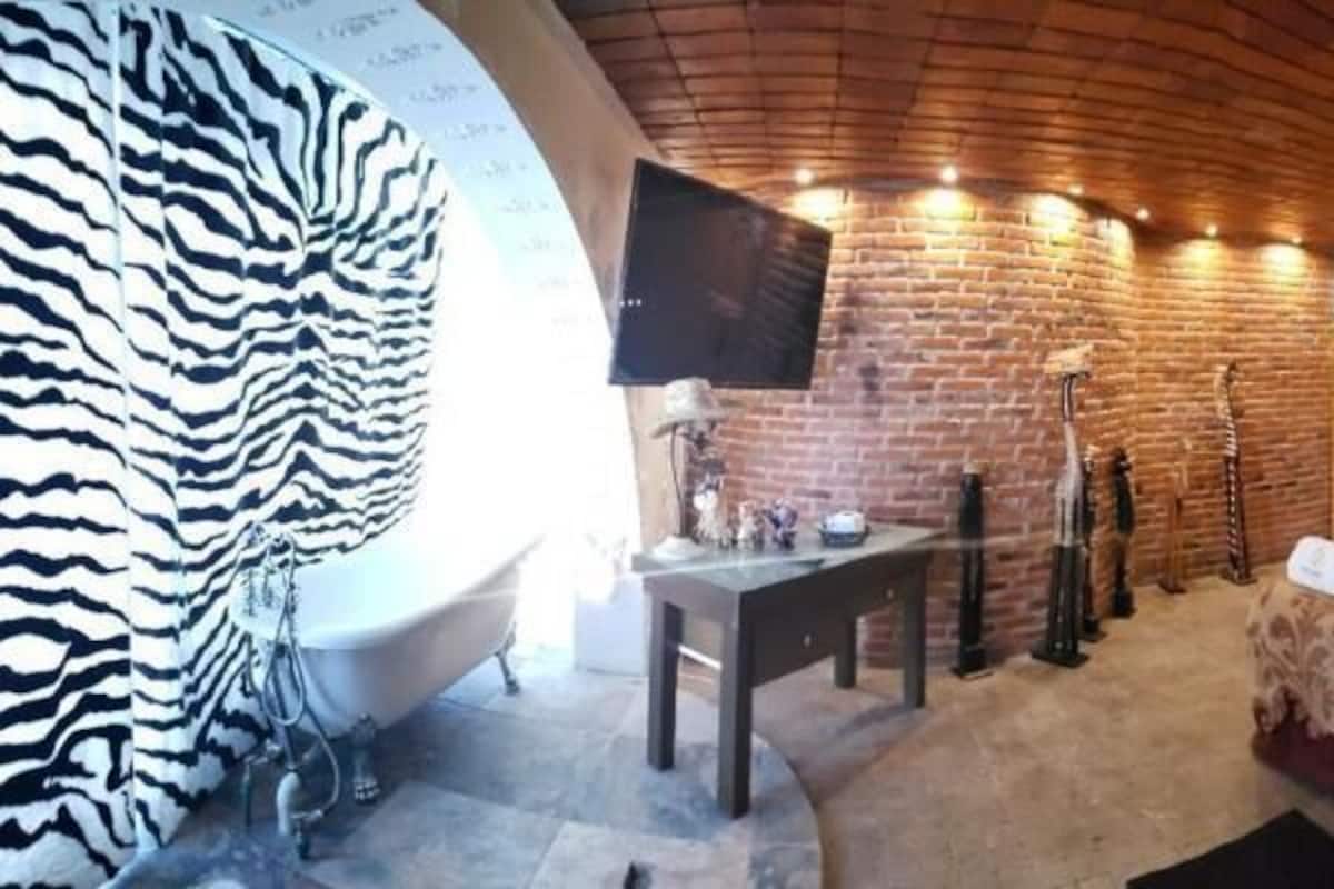 A room with a brick wall, a bed with a zebra-patterned headboard, a bathtub, and a television mounted on the wall.