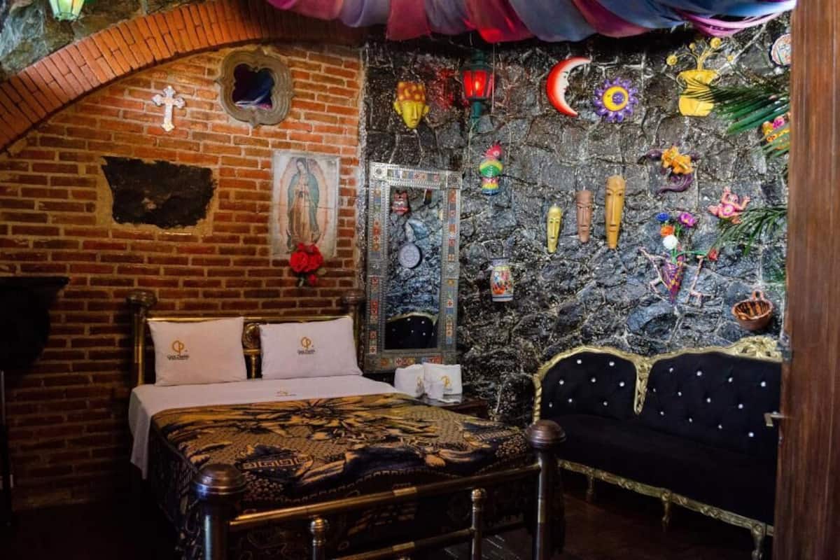 A room with a brick wall, a bed with a patterned bedspread, a dark blue sofa, and various decorative items on the wall.