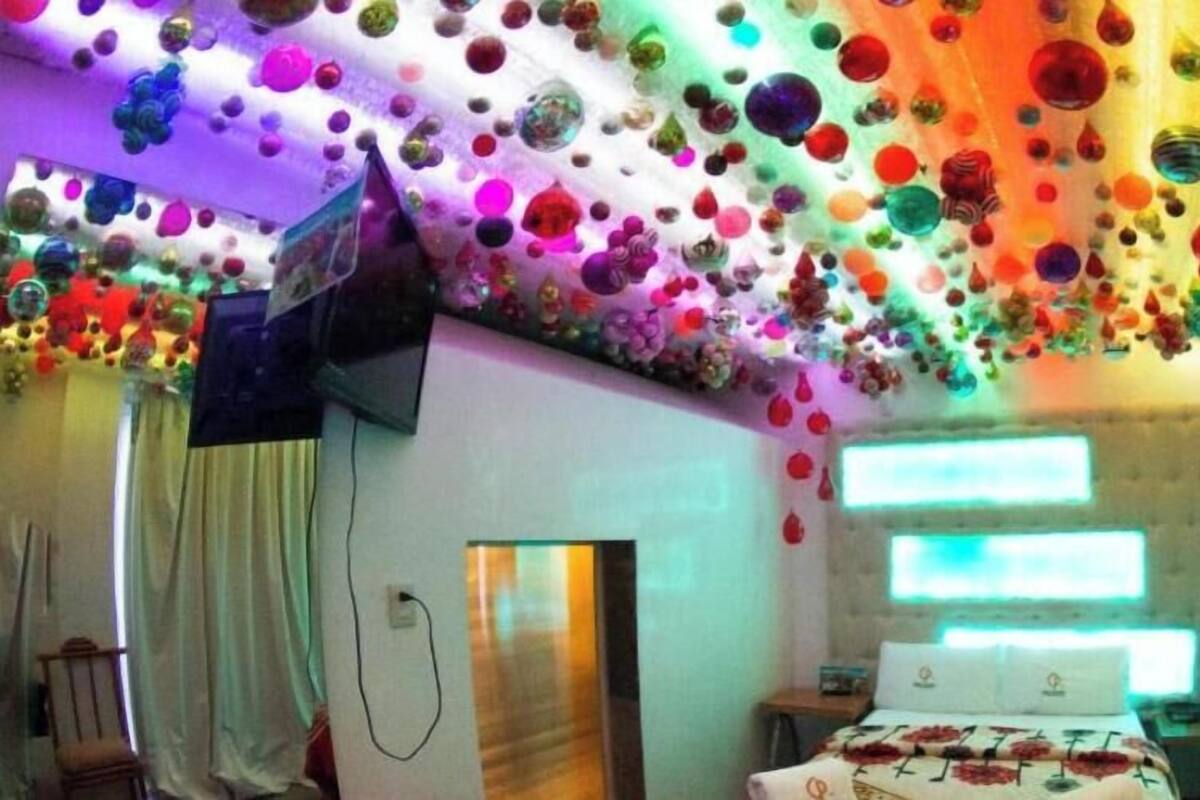 A hotel room with a bed, a nightstand, a chair, and a ceiling decorated with colorful glass orbs.