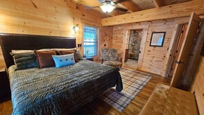 Um quarto de cabana de madeira aconchegante, com uma cama grande, uma cadeira e uma mesinha.