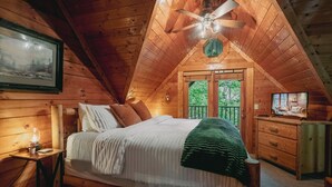 Une chambre confortable avec un plafond en bois, un lit avec des oreillers, une table de chevet, une commode et un téléviseur.