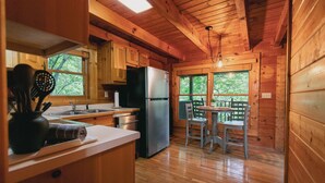 Une cuisine rustique, située dans une cabane en bois, équipée d’un réfrigérateur, d’un évier et de meubles de rangement en bois.