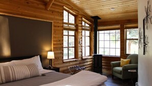 Ein Schlafzimmer in einer Blockhütte mit einem Bett, einem Sessel, einem Tisch und einem Kamin.