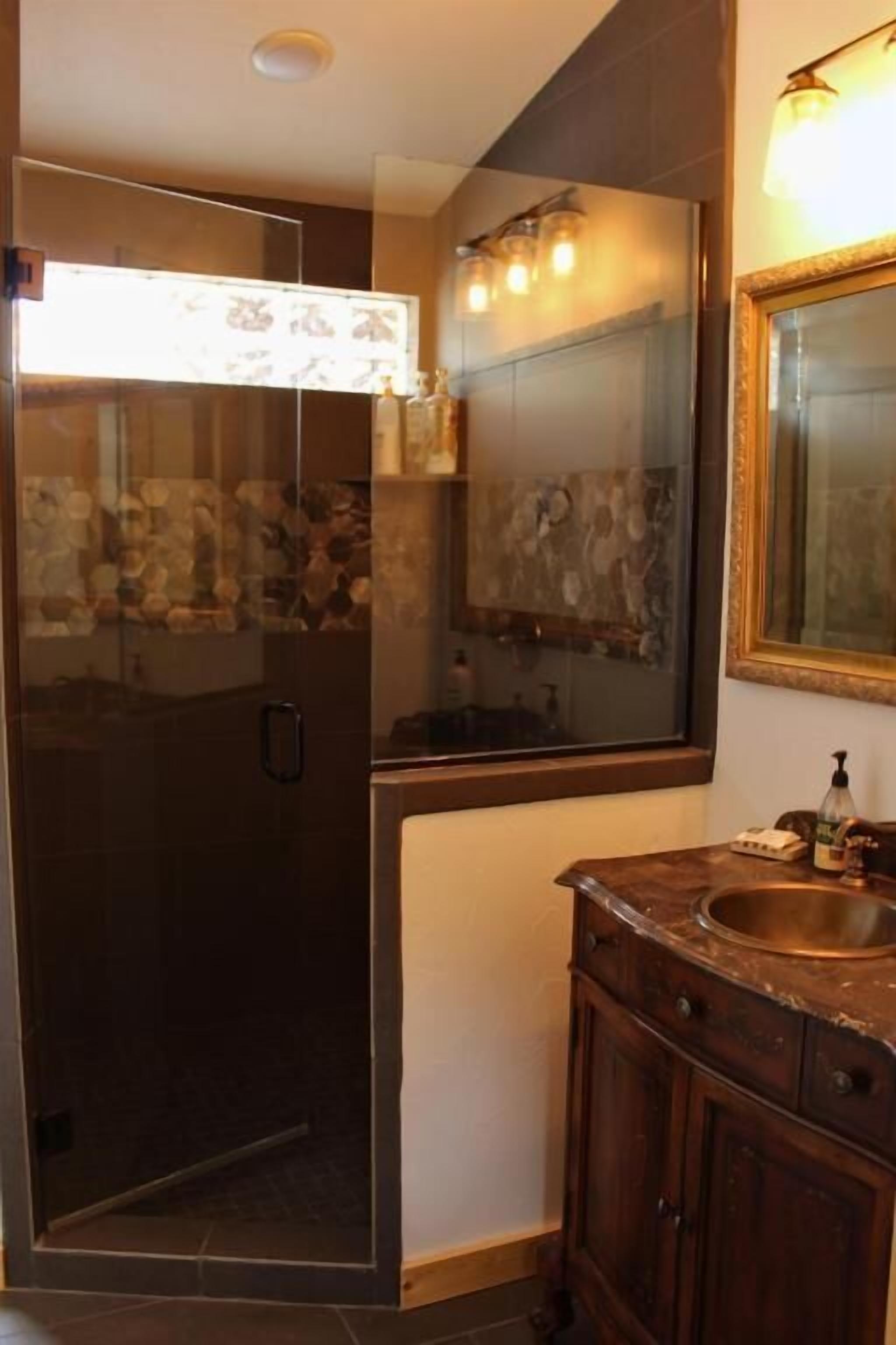 Un bagno con cabina doccia in vetro, uno specchio grande e mobili in legno.