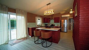 A modern kitchen with a central island, bar stools, and a large window with curtains. - Vino Villa | Cozy Escape near Wineries & Lake (Coloma)
