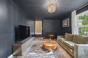 Una sala de estar moderna con televisor de pantalla plana, chimenea, sofá y alfombra estampada.